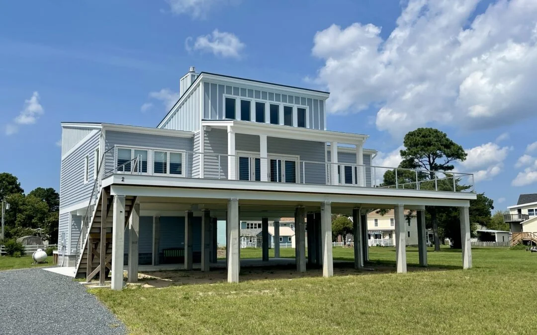 Two-story coastal stilted house featuring light gray siding and white balcony railings