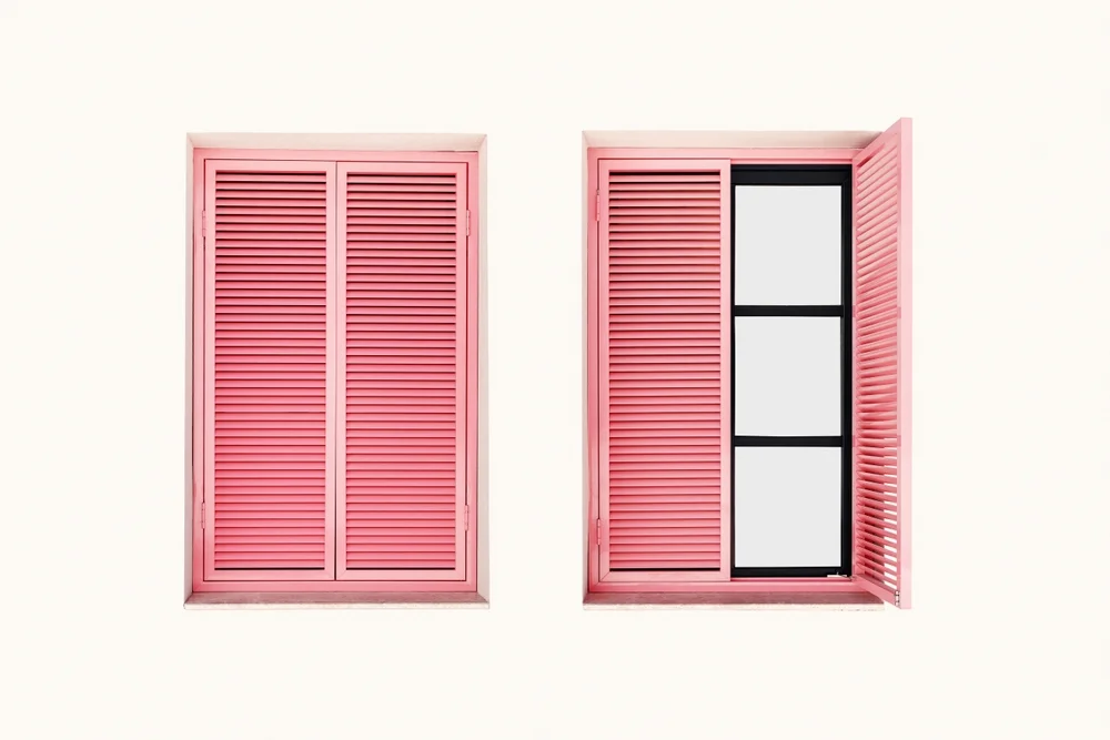 Pink window shutters on a white wall with open and closed frames